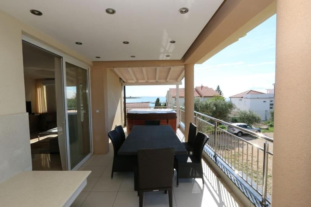 Een balkon met een tafel, stoelen, een schuifpui en uitzicht op zee en gebouwen.
