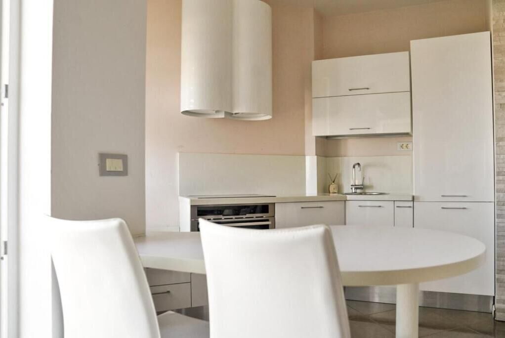 Uma cozinha moderna com armários brancos, uma mesa de jantar redonda e duas cadeiras.