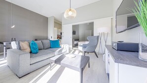 En moderne stue med en grå sofa, et sofabord og et fjernsyn på et træmøbel.