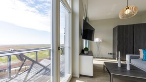 A modern living room with a large TV, a sofa, a coffee table, and a balcony with a view.