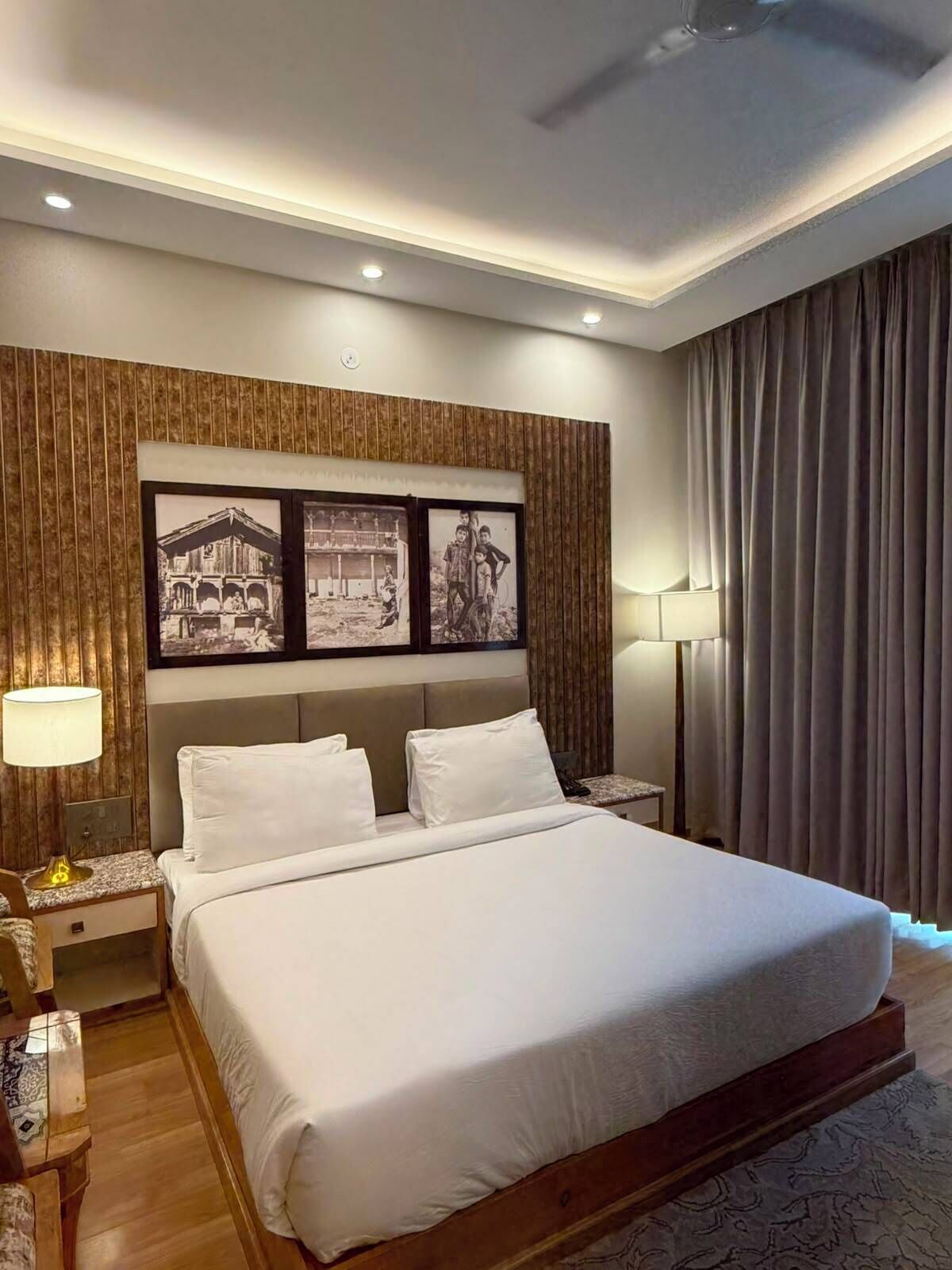 A modern hotel room with a large bed, wooden paneling on the walls, and framed black-and-white photographs.