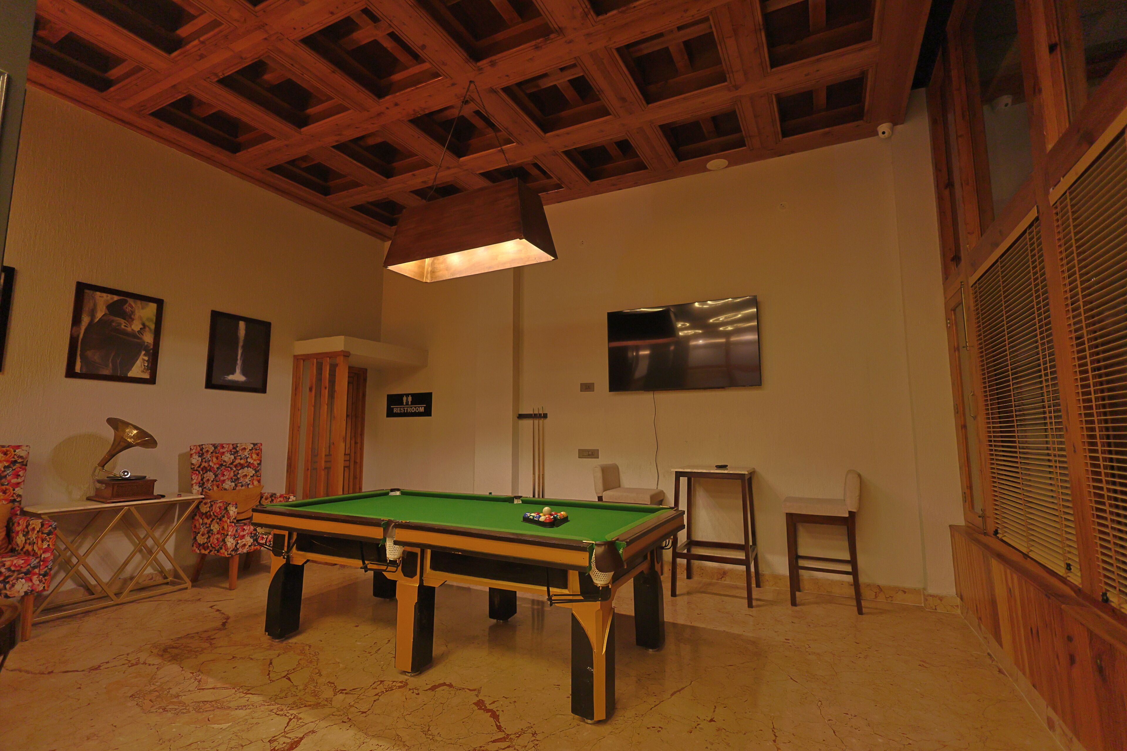 A billiards table in a room with wooden beams on the ceiling, a television, and framed pictures on the wall.