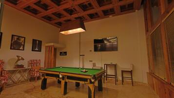 A billiards table in a room with wooden beams on the ceiling, a television, and framed pictures on the wall.