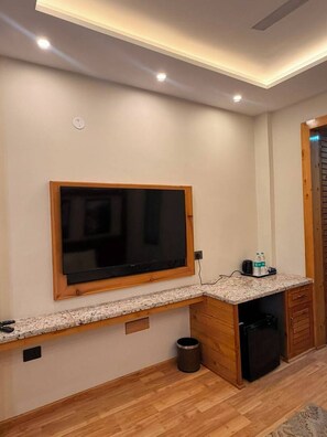 A kitchen with a built-in TV, wooden cabinets, a granite countertop, and a trash can. - The Uttrayan (Chakrata)