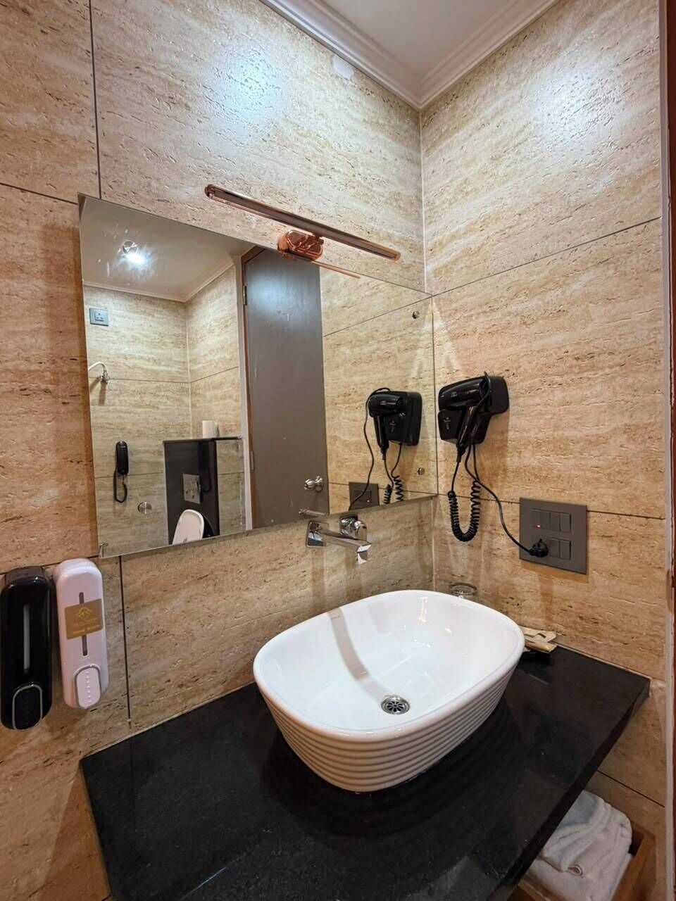 A bathroom with a large mirror, a sink, a hairdryer, and a telephone.