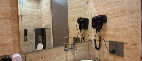 A bathroom with a large mirror, a sink, a hairdryer, and a telephone.