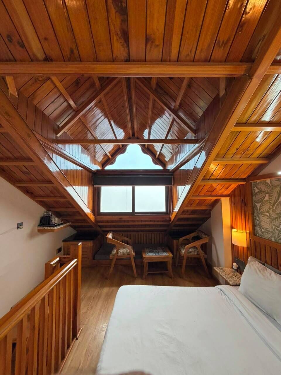A high-ceilinged room with a sloped roof, wooden beams, a bed, a desk, and a chair.