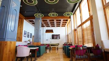 A restaurant interior with wooden beams, green circular ceiling lights, and a TV mounted on the wall.