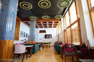 A restaurant interior with wooden beams, green circular ceiling lights, and a TV mounted on the wall.