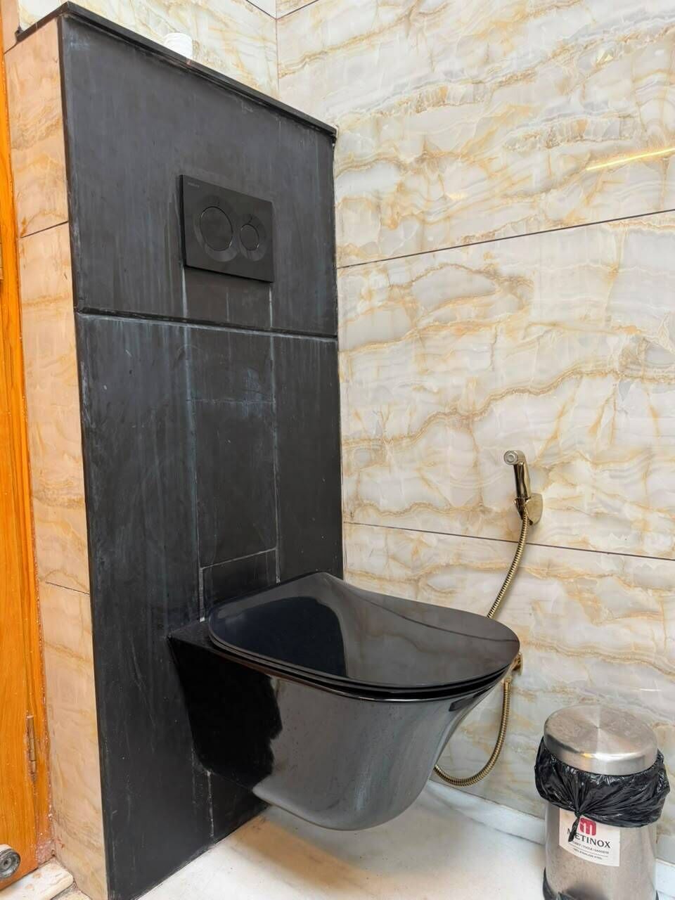 A bathroom with a black toilet, marble walls, and a trash bin.