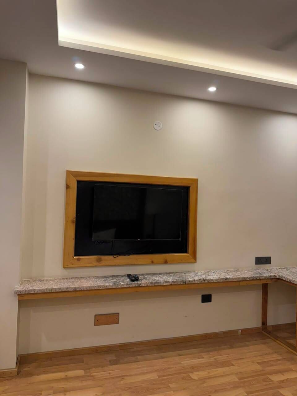 A room with a wooden-framed window, a built-in bench with a countertop, recessed ceiling lighting, and a wooden floor.
