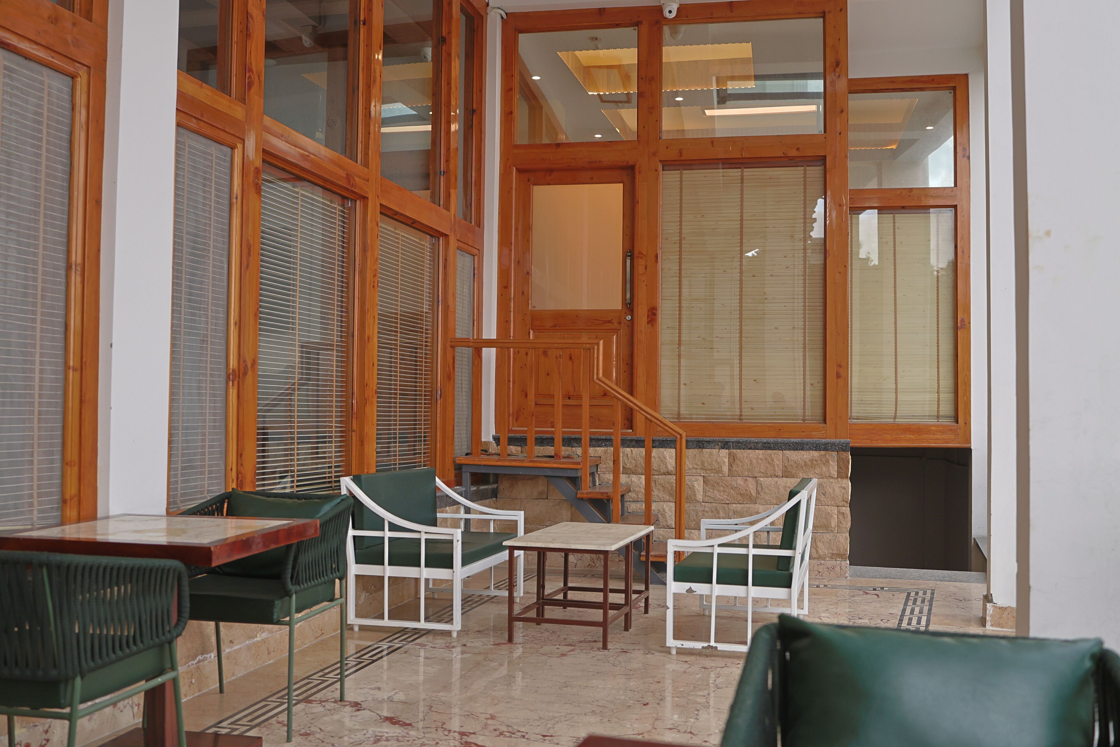 A room with a wooden staircase, green chairs, a table, and large windows with blinds.