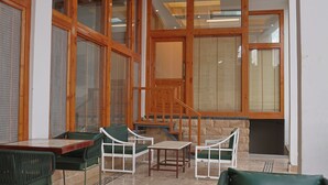 A room with a wooden staircase, green chairs, a table, and large windows with blinds. - The Uttrayan (Chakrata)