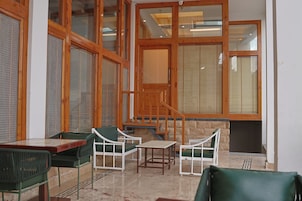 A room with a wooden staircase, green chairs, a table, and large windows with blinds.