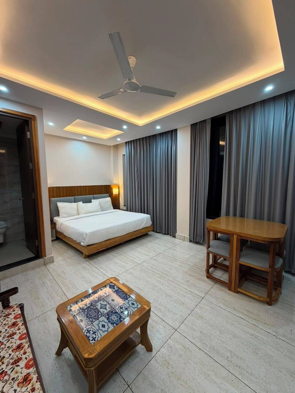 Ein Hotelzimmer mit Bett, Tisch, Couchtisch, Deckenventilator und Vorhängen.