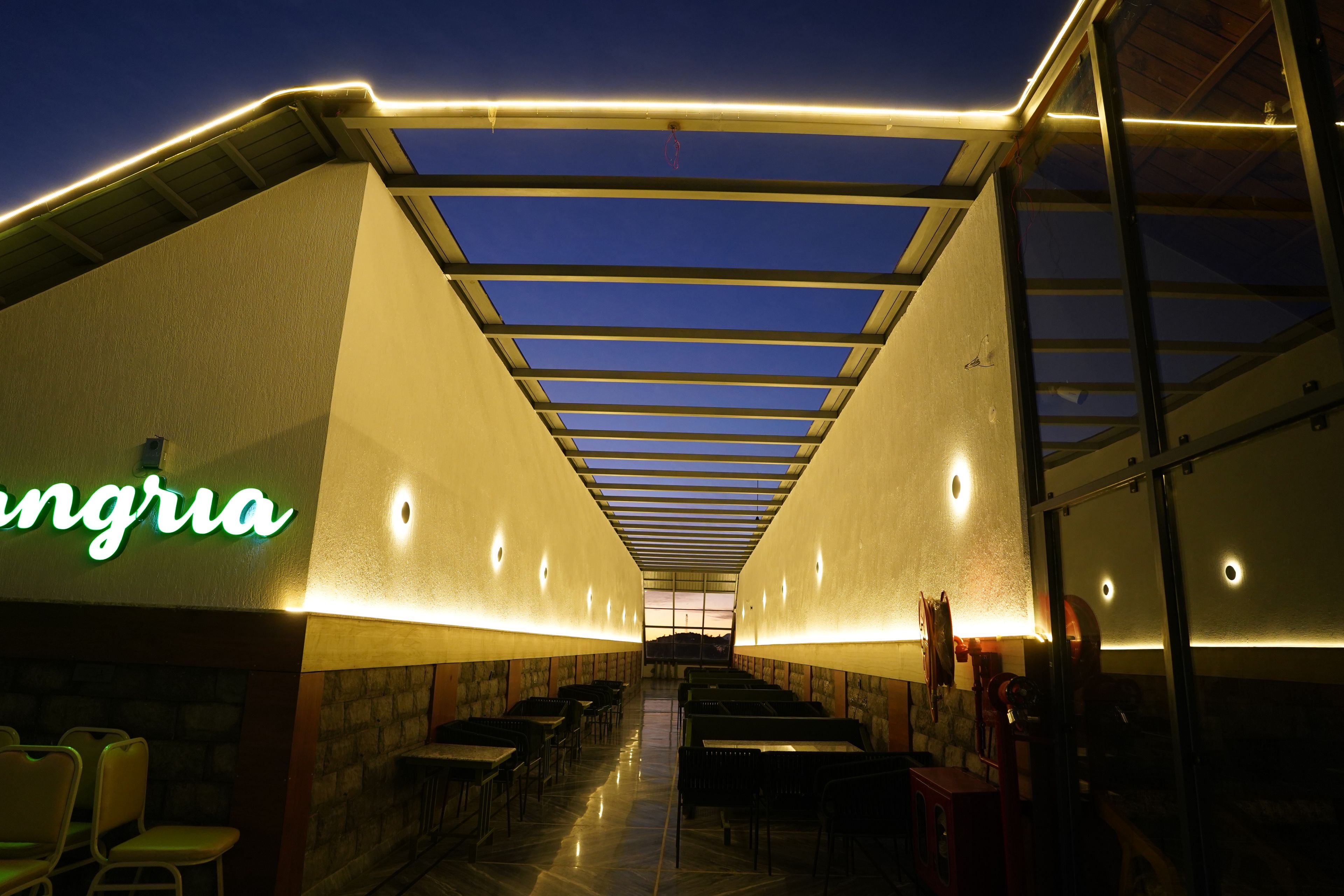 A restaurant with a long counter, chairs, and a neon sign.
