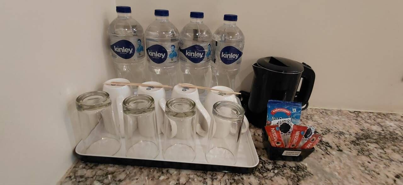 En køkkenbordplade med vandflasker, en kaffemaskine og en bakke med glas.