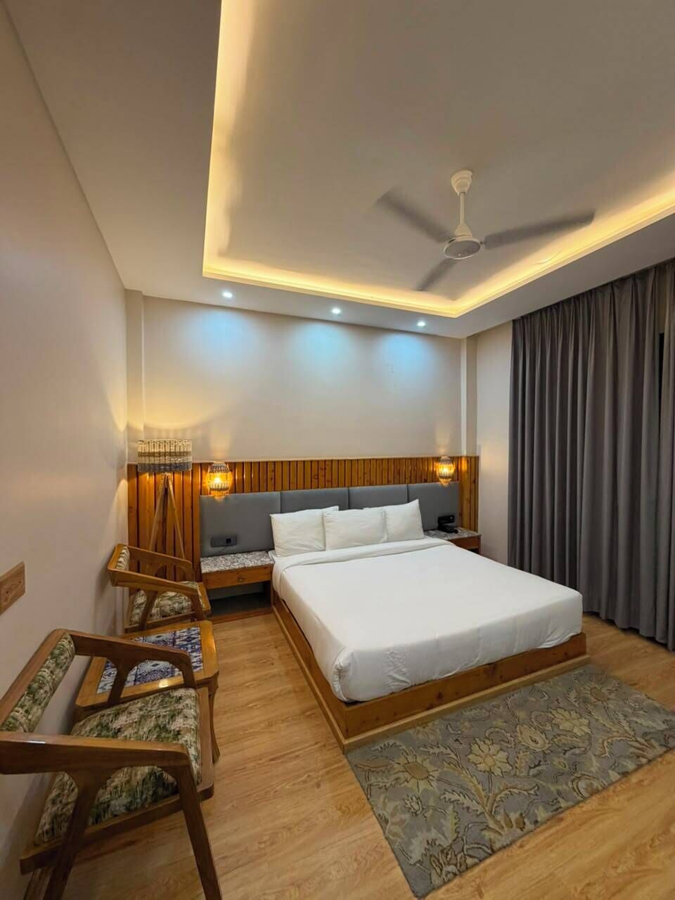 A hotel room with a bed, bedside table, lamp, chair, and a ceiling fan.