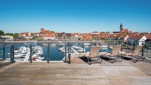 A marina with boats, a waterfront promenade with lounge chairs, and historic buildings in the background.