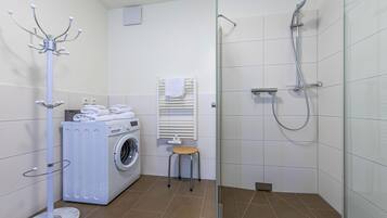 Une salle de bain moderne équipée d’un lave-linge, d’un porte-serviettes, d’une cabine de douche en verre et d’un petit tabouret.