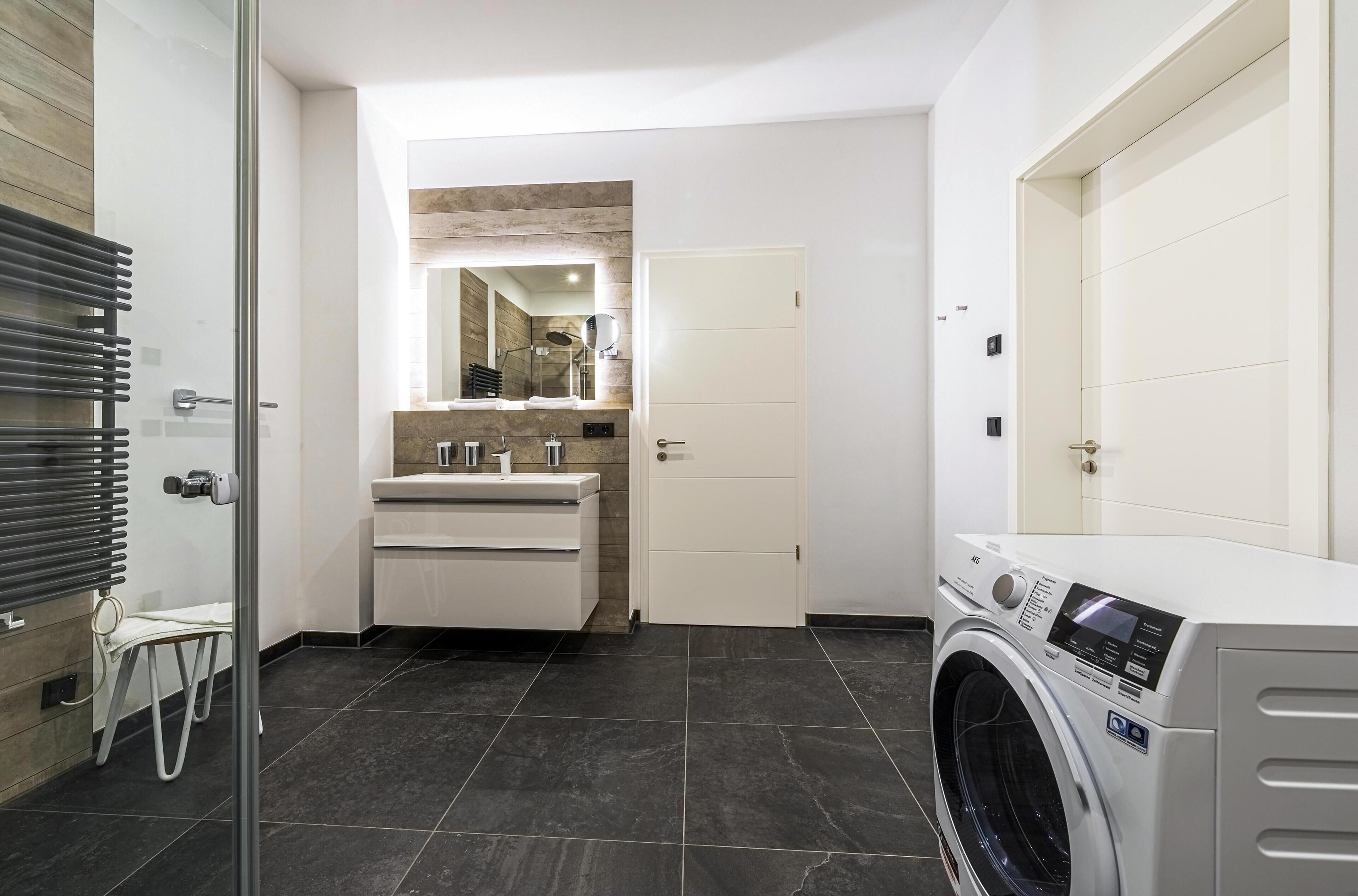 A modern bathroom with a glass shower enclosure, a built-in sink, and a front-loading washing machine.