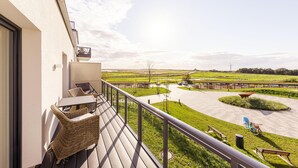 Een balkon met rieten meubilair, met uitzicht op een parkeerplaats en velden.
