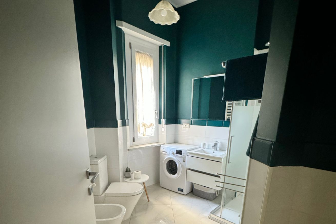 Ein kleines Badezimmer mit Toilette, Waschmaschine, Waschbecken und Spiegel.