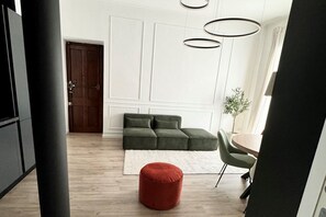 Una sala de estar moderna con un sofá seccional, un reposapiés rojo, una mesa redonda y una planta en maceta.