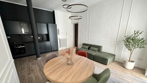 A modern kitchen with dark cabinets, a round wooden table, and a green sofa in a bright living area. - GuestHost - 65 sqm apartment for 4 people, located on the second floor of a building without an elevator, featuring a balcony. Situated in the Lingotto neighborhood, a convenient and well-served area, close to the Regina Margherita Hospital and just minu (Torino)