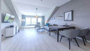 Un salon moderne comprenant un coin repas, un canapé, une table basse et un téléviseur posé sur un meuble.