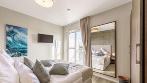 Ein Schlafzimmer mit Bett, Kissen, Fernseher, einem großen Fenster und einem Spiegel, der den Raum widerspiegelt.