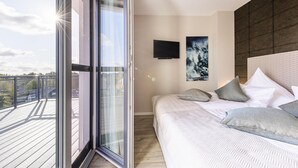 Ein Schlafzimmer mit großem Fenster, einem Bett mit Kissen, einem Wand-Fernseher und einem Bild an der Wand.