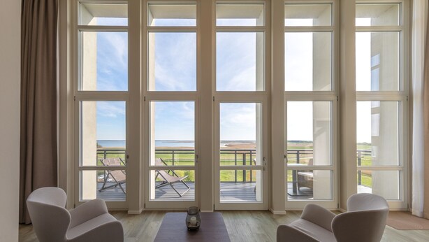 Una habitación con ventanas amplias, un sofá, dos sillones y una mesa con una vela.