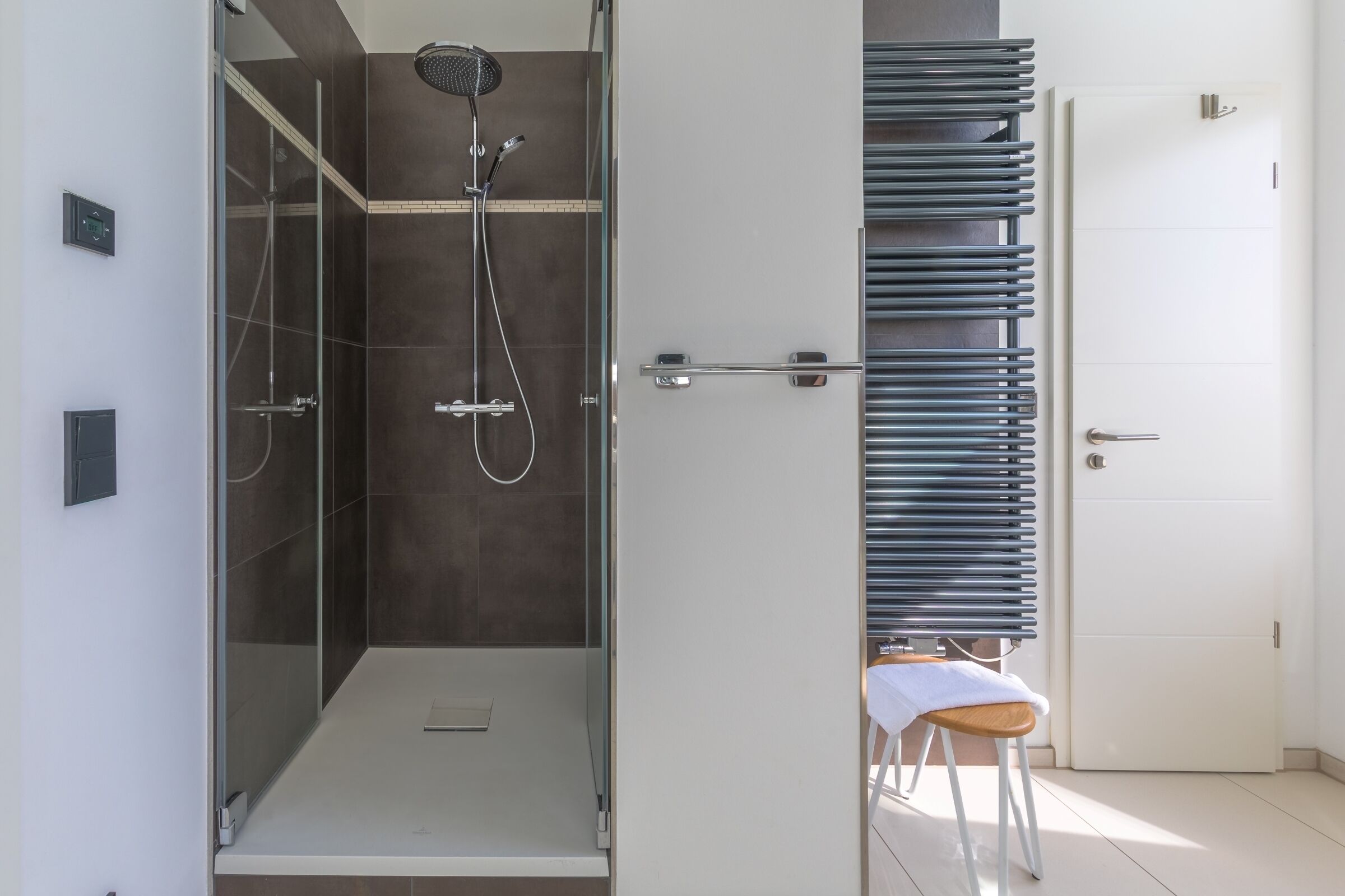 A modern bathroom with a glass-enclosed shower, a white door, and a towel rack.