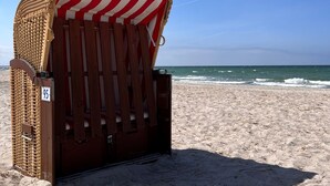 Una silla de playa con toldo a rayas, ubicada en una playa arenosa con el océano al fondo.
