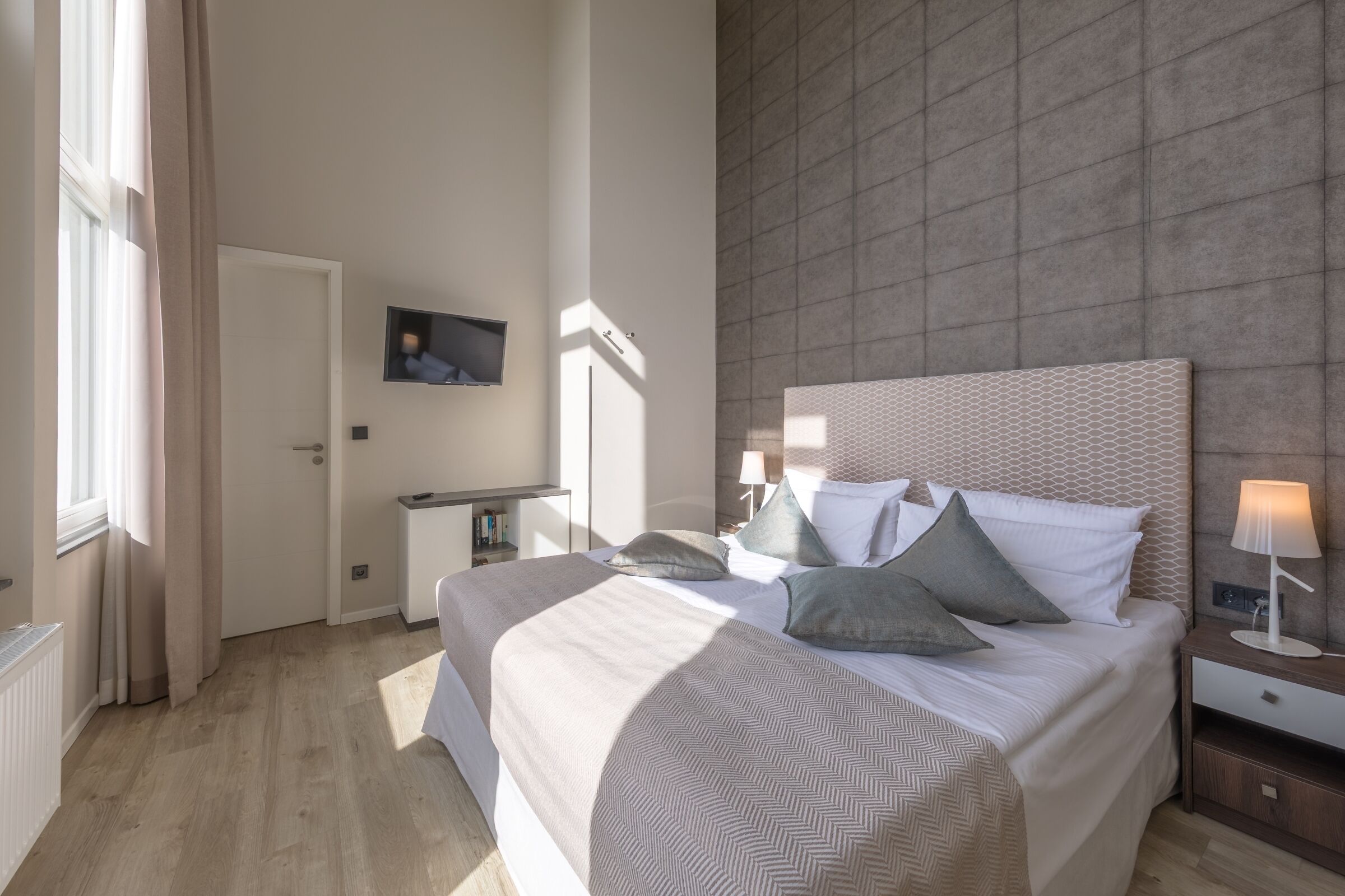 A modern bedroom with a large bed, bedside tables, a nightstand, and a wall-mounted TV.