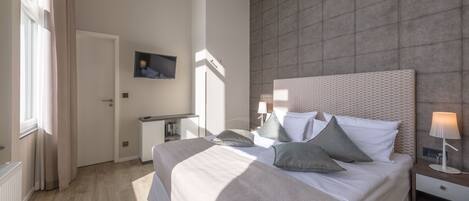 A modern bedroom with a large bed, bedside tables, a nightstand, and a wall-mounted TV.