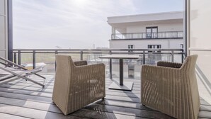A balcony with wicker chairs and a table, overlooking a building with a balcony.