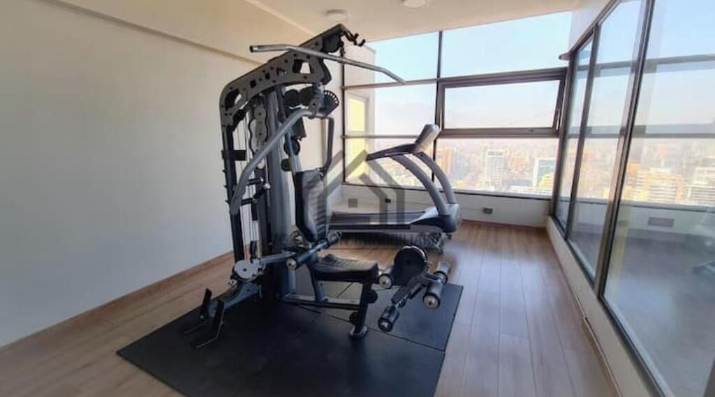 Une salle de sport équipée de tapis de course et d’appareils de musculation, dotée de grandes fenêtres et offrant une vue sur la ville.