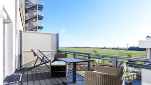 Ein Balkon mit Korbmöbeln, einem Tisch und Blick auf eine grüne Landschaft.