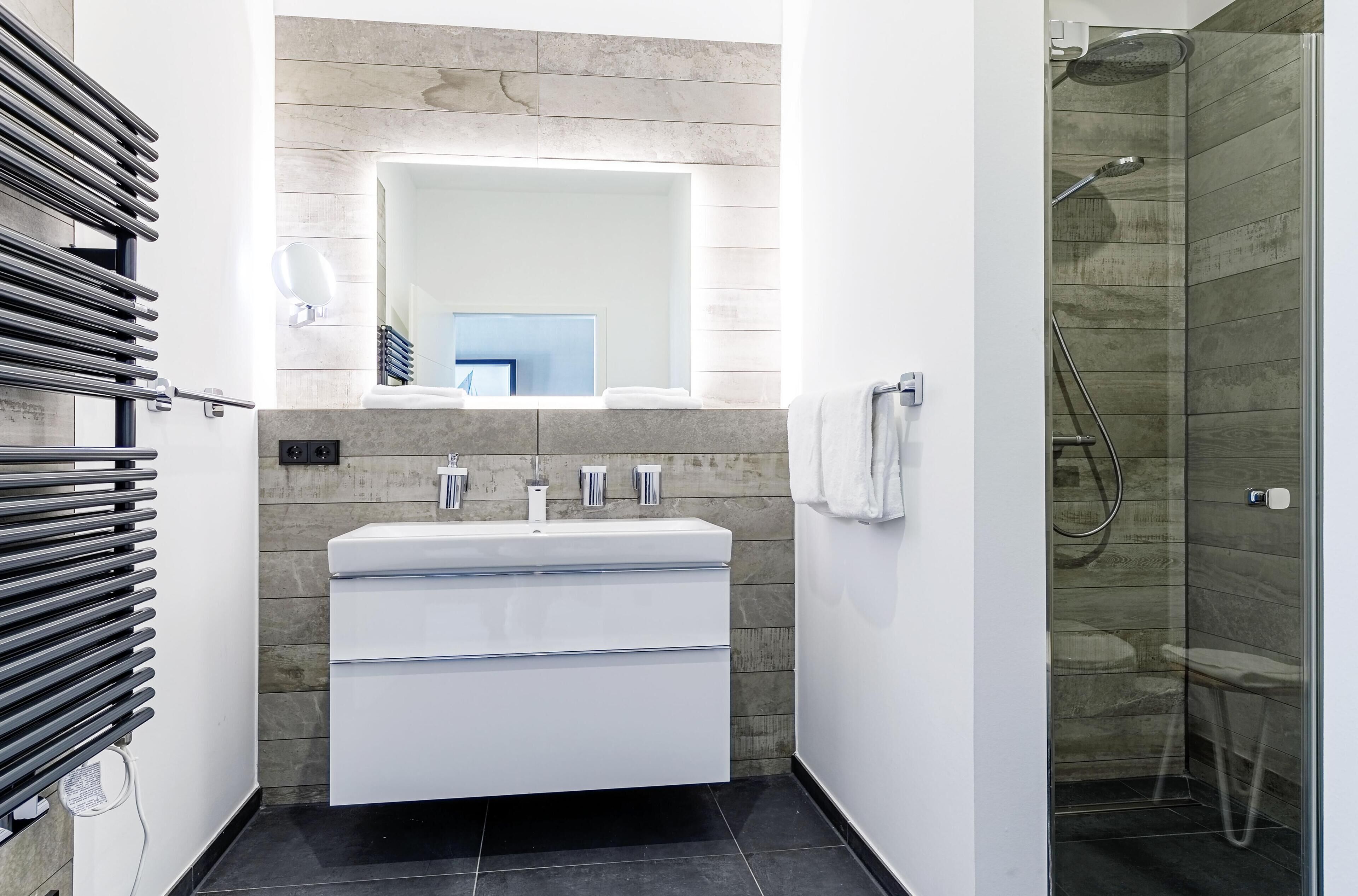 A modern bathroom with a white sink, mirror, and shower.