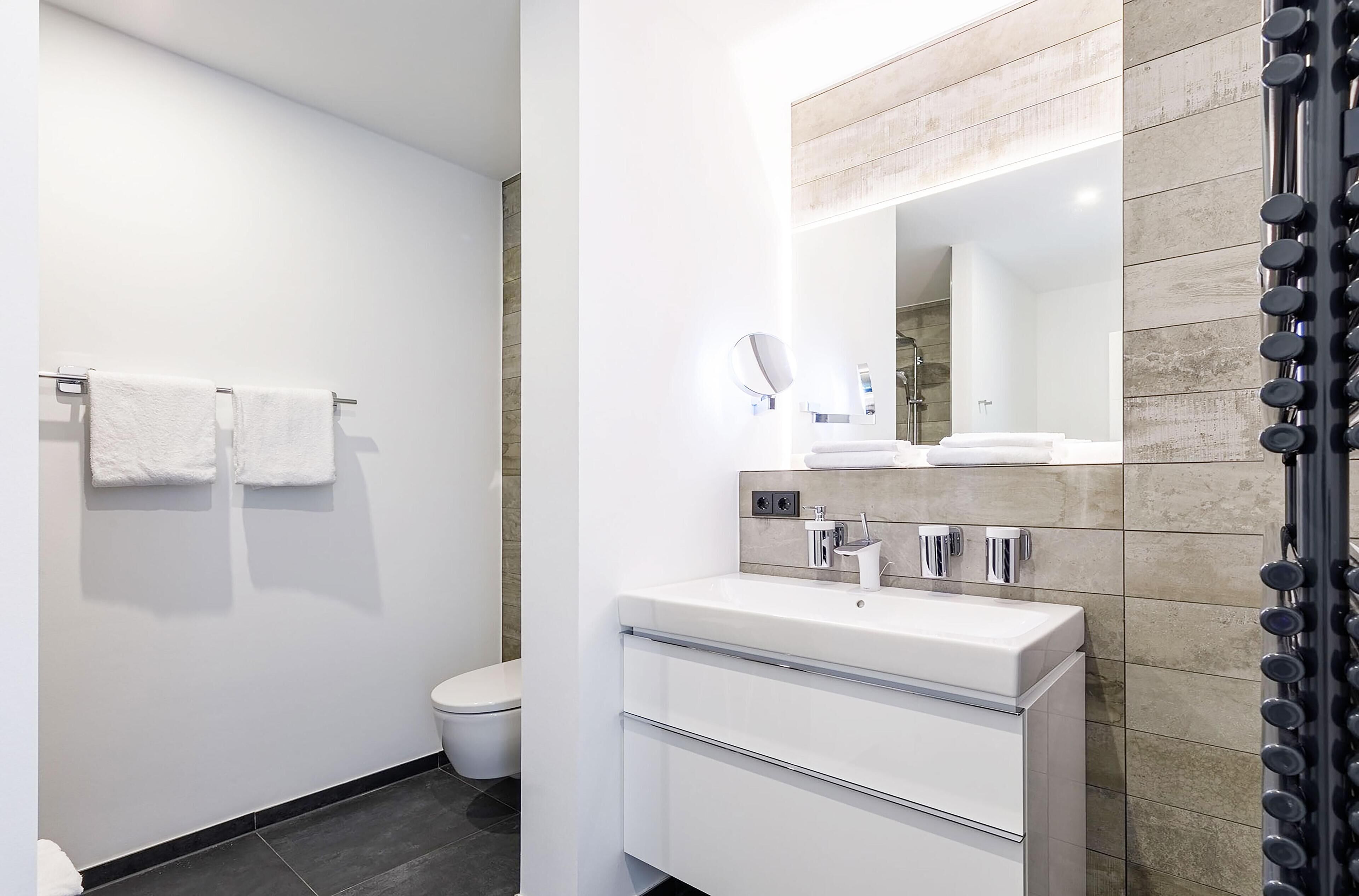 A modern bathroom with a white sink, mirror, and towel rack.
