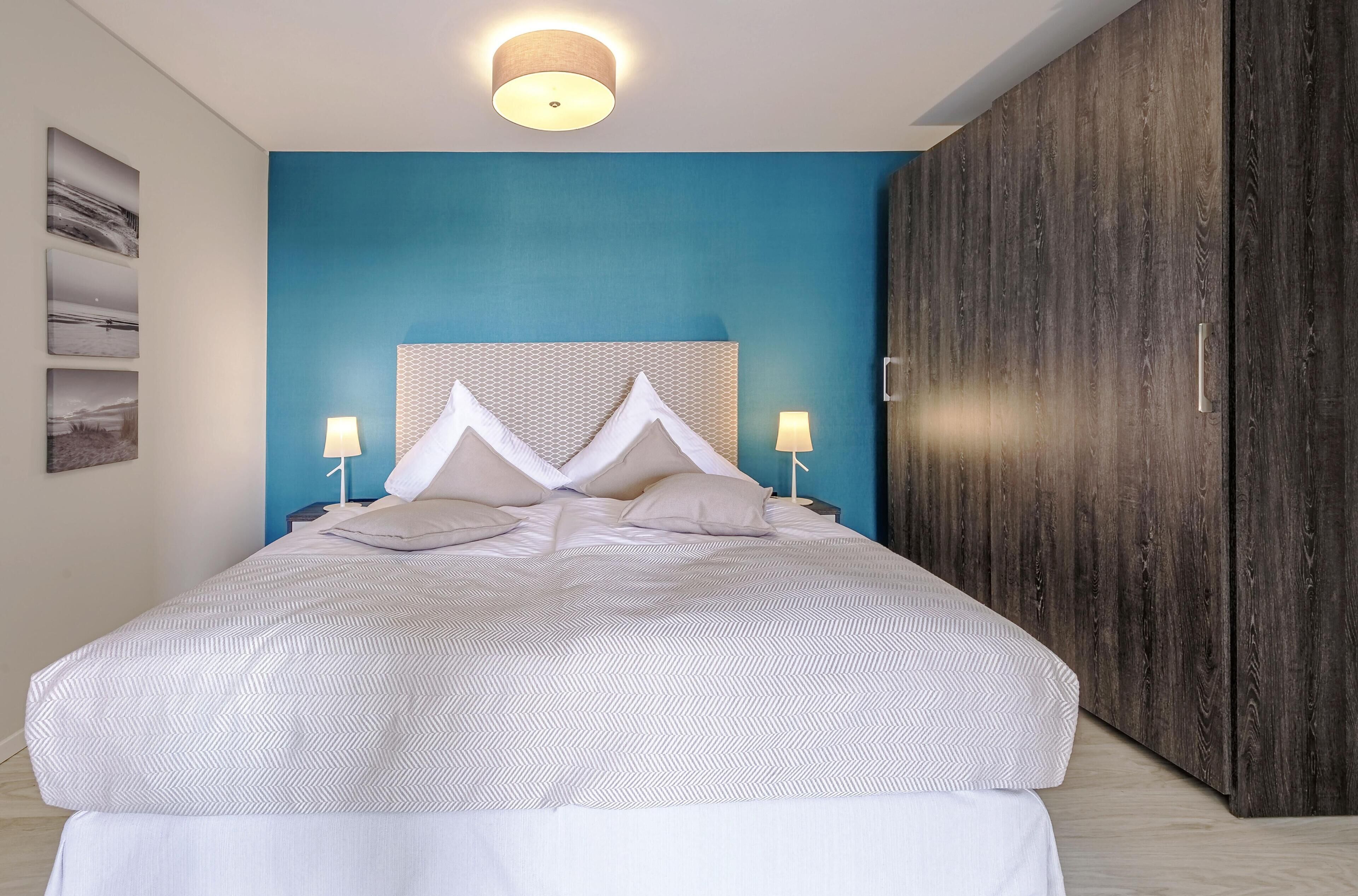 Un dormitorio moderno con una cama grande, una pared azul de acento y un armario de madera.