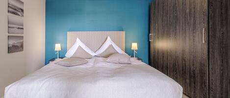 Un dormitorio moderno con una cama grande, una pared azul de acento y un armario de madera.