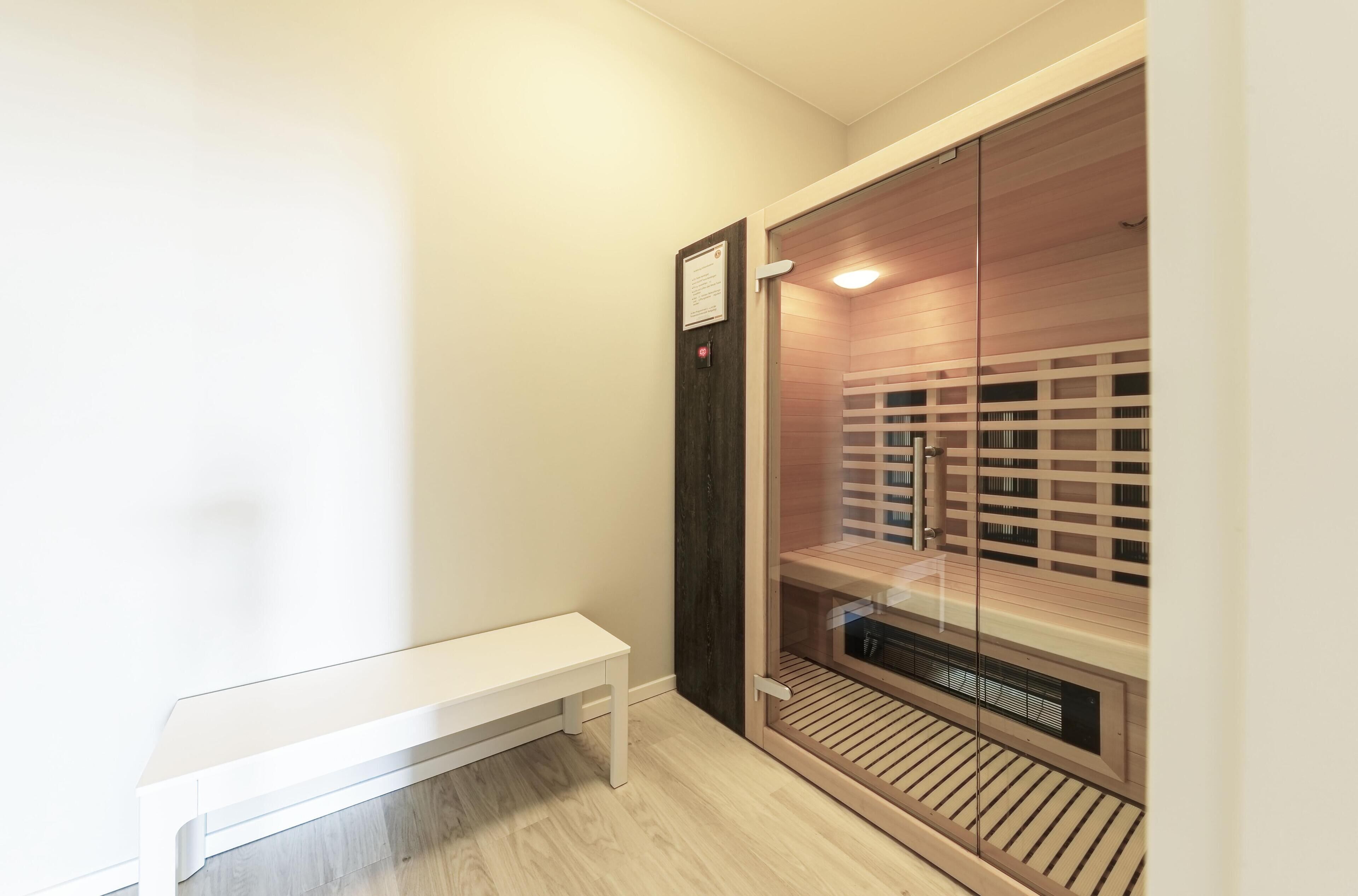 A sauna room with a bench, wooden slats, and a glass door.