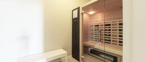 A sauna room with a bench, wooden slats, and a glass door.