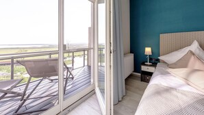 Un dormitorio con una ventana grande, una cama, una mesita de noche y una silla en un balcón.