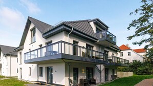 A modern two-story house with a balcony, a patio with outdoor furniture, and a well-maintained lawn. - 5-star vacation apartment "Seeblick" with east-facing balcony (Wustrow)