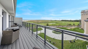 Ein Balkon mit Korbmöbeln, Blick auf eine grüne Landschaft mit einer Straße und einem Gebäude im Hintergrund.