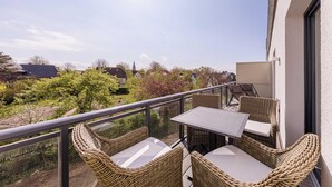 A balcony with wicker furniture and a laptop, overlooking a garden and buildings. - Humboldtsuite Wustrow - 5 stars, wellness, balcony & underground parking (Wustrow)